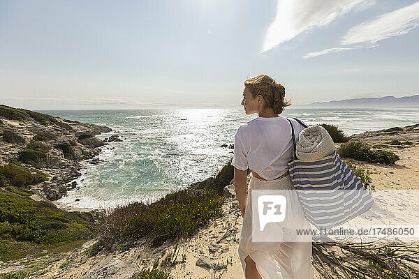 Teenage girl standing on top of a cliff looking over the coastline and inlet.