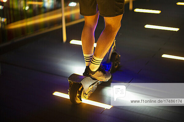 Mann fährt Roller auf beleuchtetem Gehweg bei Nacht