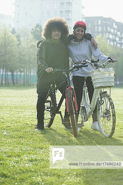 Porträt glückliches Teenager-Paar auf Fahrrädern im städtischen Park Gras