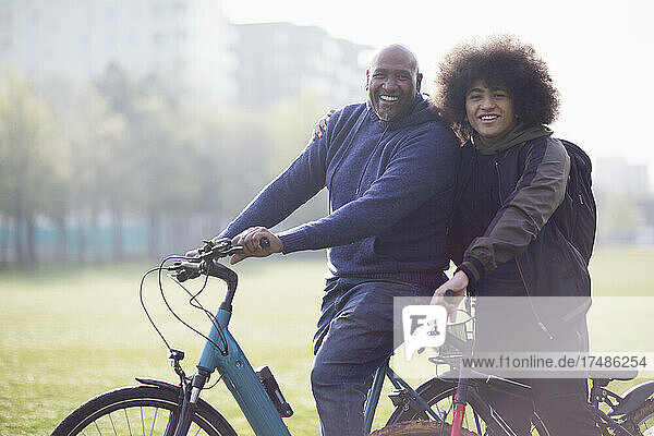 Portrait happy father and teen son on bicycles in urban park