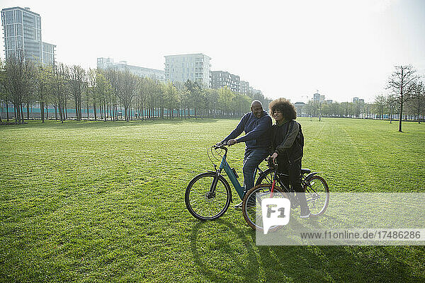 Vater und Sohn fahren mit dem Fahrrad auf dem Rasen eines sonnigen Stadtparks