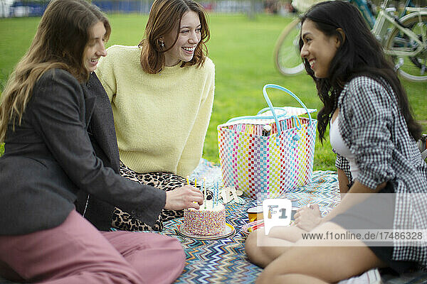 Glückliche junge Frauen Freunde feiern Geburtstag mit Kuchen im Park