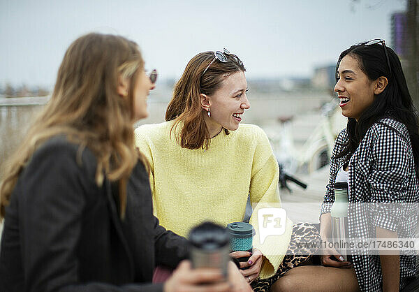 Happy young women friends talking and drinking coffee