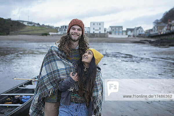 Portrait glückliches junges Paar eingewickelt in eine Decke am Winterstrand