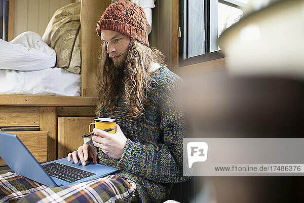 Junger Mann benutzt Laptop in einer kleinen gemieteten Hütte