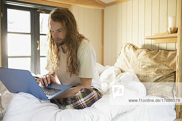 Junger Mann mit Laptop im Bett