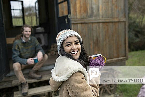 Glückliche junge Frau trinkt Kaffee vor einer kleinen gemieteten Hütte