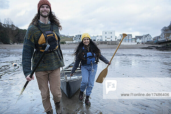 Happy young couple pulling canoe on wet sand beach