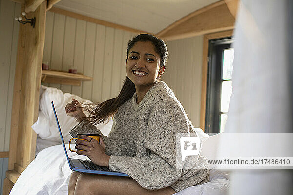 Portrait happy young woman using laptop in bed