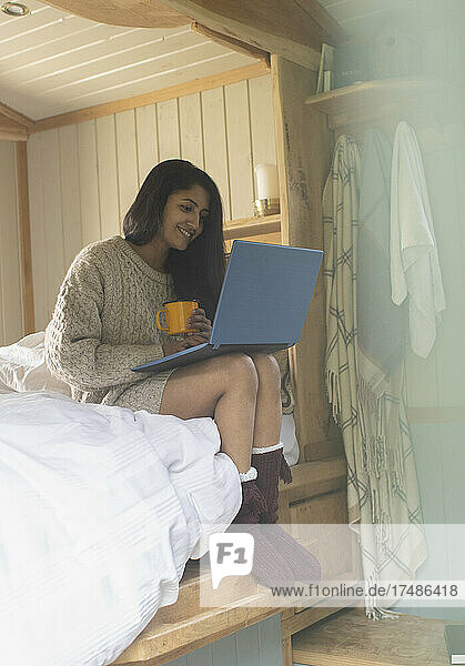 Young woman using laptop in tiny cabin rental bed