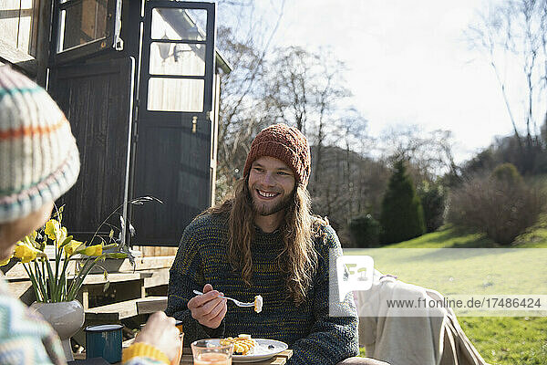 Glücklicher junger Mann beim Frühstück vor einer winzigen gemieteten Hütte