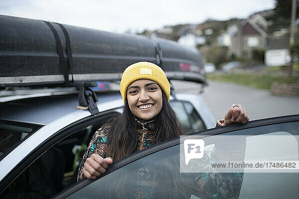 Porträt einer glücklichen jungen Frau  die in ein Auto mit einem Kanu auf dem Dach steigt