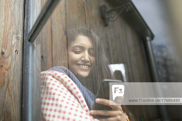 Lächelnde junge Frau mit Smartphone im Fenster