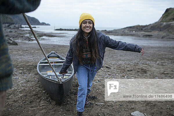 Porträt einer glücklichen jungen Frau  die ein Kanu am Strand zieht