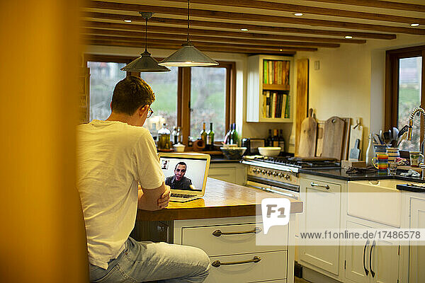 Mann hält Videokonferenz mit Kollegen am Laptop in der Küche