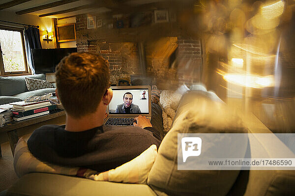 Mann bei einer Videokonferenz mit Kollegen am Laptop auf dem Sofa