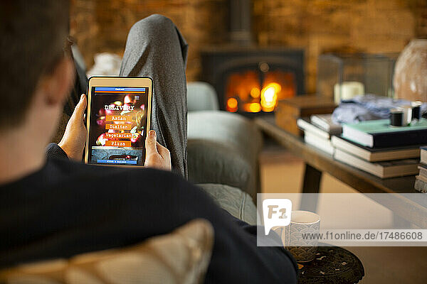 Mann betrachtet Speisekarte zum Mitnehmen auf digitalem Tablet im Wohnzimmer