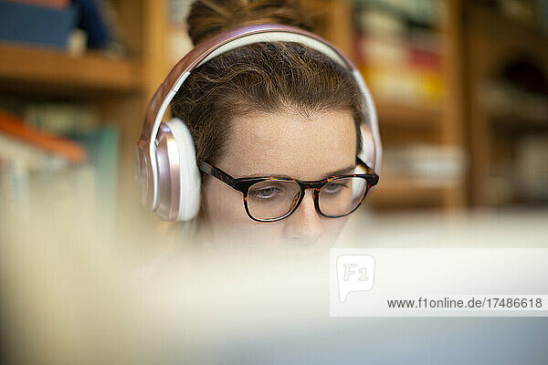 Konzentrierte Frau mit Kopfhörern und Brille  die von zu Hause aus arbeitet