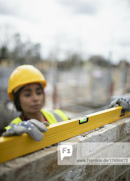 Bauarbeiterin mit Nivelliergerät an einer Ziegelmauer