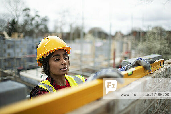 Bauarbeiterin mit Nivelliergerät an einer Ziegelmauer
