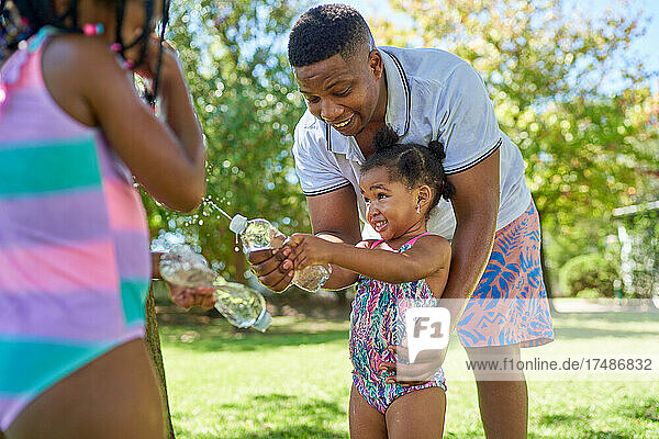 Vater und Töchter spielen mit einer Wasserflasche im Hinterhof