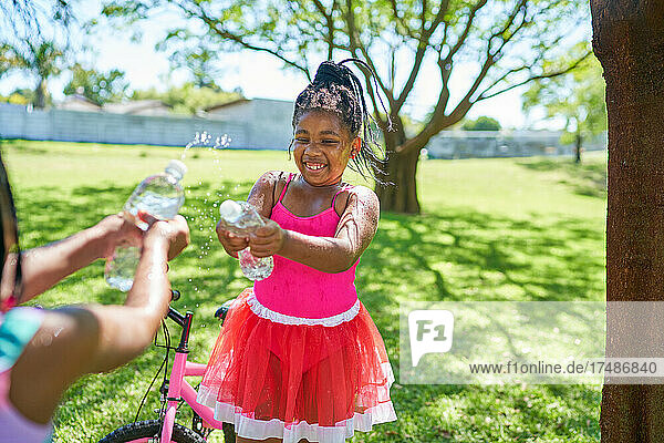 Glückliche Mädchen spielen mit Wasserspritzflaschen im Sommerpark