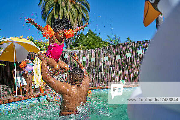 Vater wirft seine Tochter im sonnigen Sommerschwimmbad in die Luft