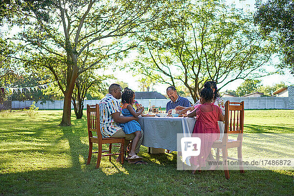 Multigenerational family enjoying lunch at table in summer backyard