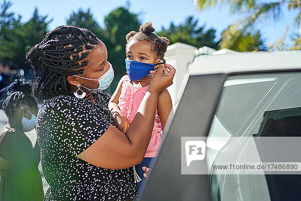 Mutter hilft Tochter mit Gesichtsmaske außerhalb des Autos