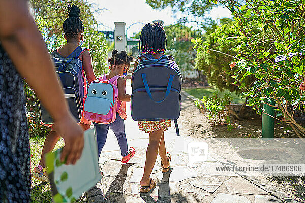 Sisters with backpacks walking on sunny summer footpath