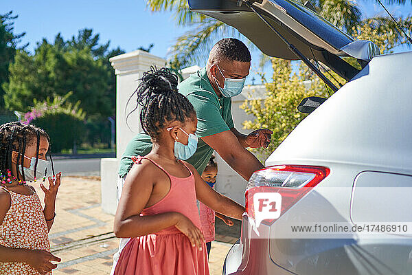 Vater und Töchter mit Gesichtsmasken beim Beladen eines Autos