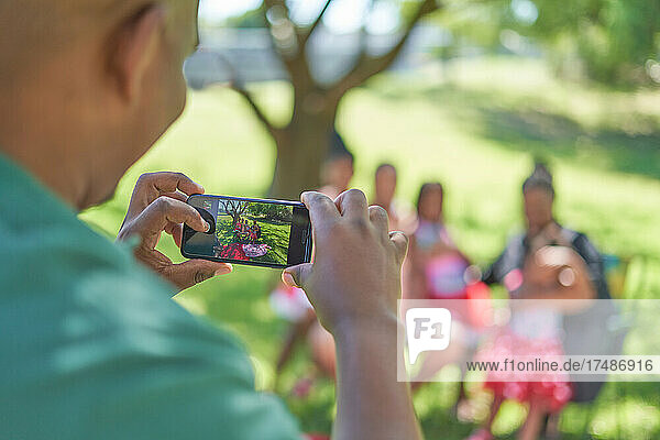 Mann fotografiert Familie mit Smartphone im Park