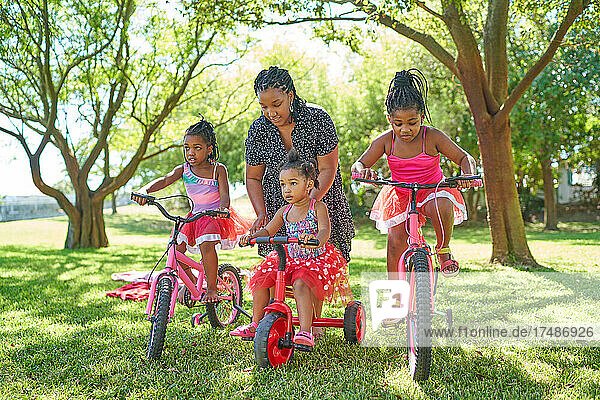 Mother and daughters with bicycles and tricycle in summer park