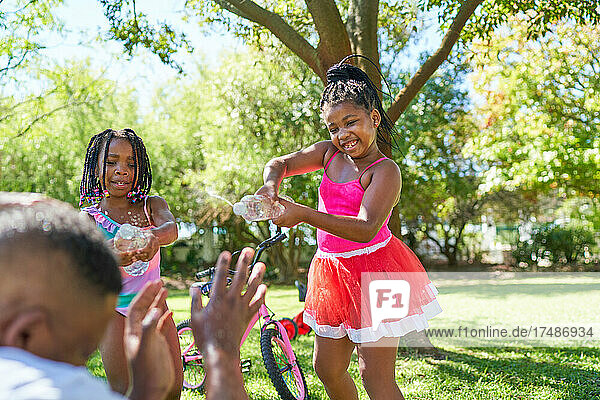 Verspielte Töchter bespritzen Vater im Sommerpark mit Wasser