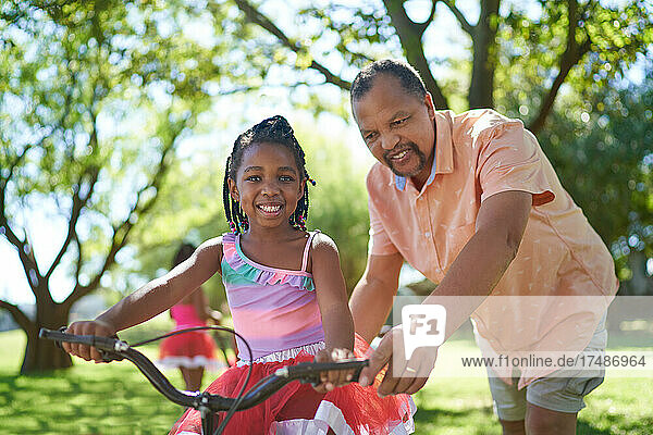 Portrait happy grandfather and granddaughter riding bike in park