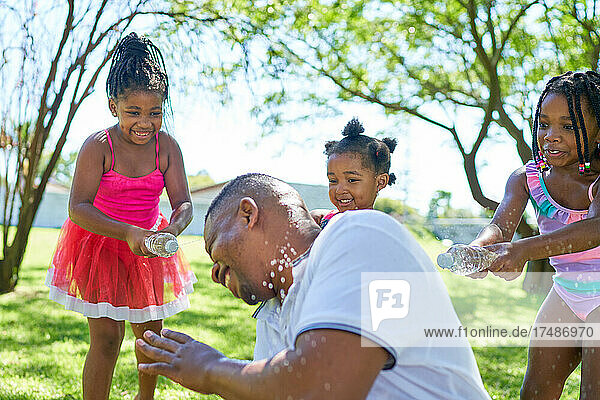 Happy playful daughters splashing father with water bottles in park