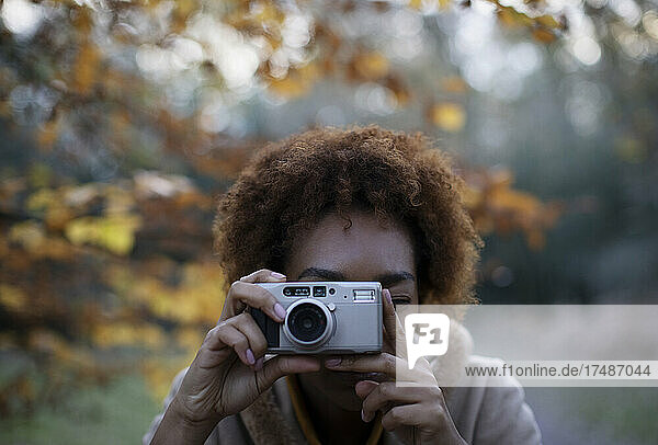 Porträt junge Frau mit Digitalkamera im herbstlichen Park