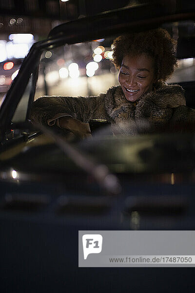 Junge Frau benutzt nachts ihr Smartphone im Cabrio