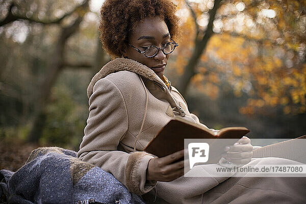 Gelassene junge Frau beim Lesen im herbstlichen Park