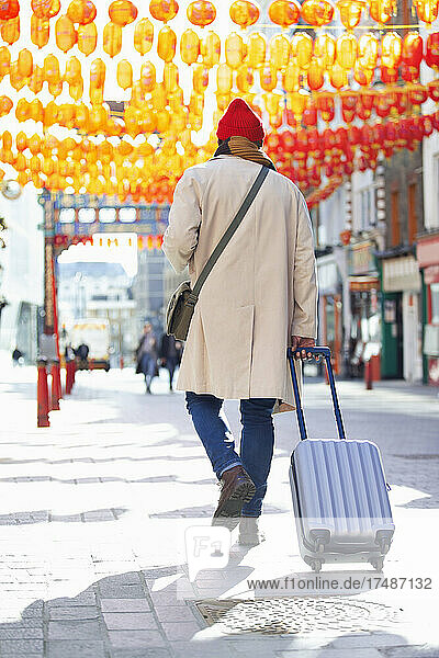 Male tourist pulling suitcase on sidewalk in Chinatown  London  UK