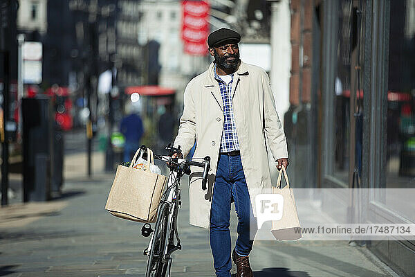 Mann mit Fahrrad und Einkaufstüten zu Fuß in sonniger Stadt