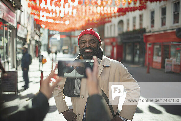 Frau mit Gesichtsmaske fotografiert glücklichen Mann auf einer sonnigen Straße in der Stadt