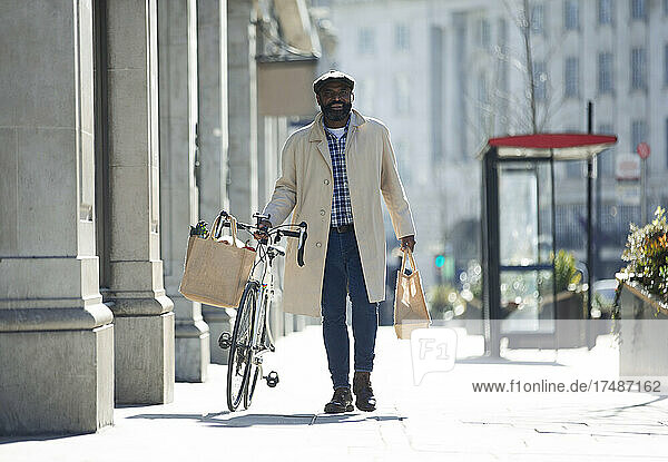 Man with. bicycle and groceries walking on sunny city sidewalk