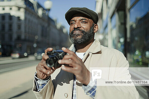 Männlicher Tourist mit Bart benutzt eine Digitalkamera auf einem sonnigen Bürgersteig