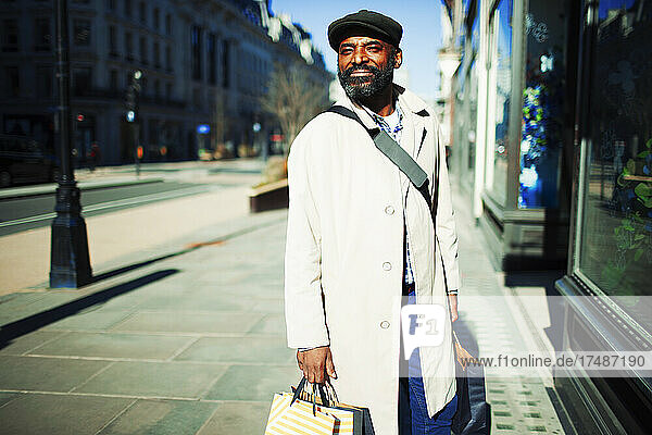 Gut aussehender Mann mit Einkaufstüten vor einem sonnigen städtischen Geschäft