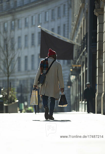 Mann mit Einkaufstüten auf sonnigem Bürgersteig in der Stadt