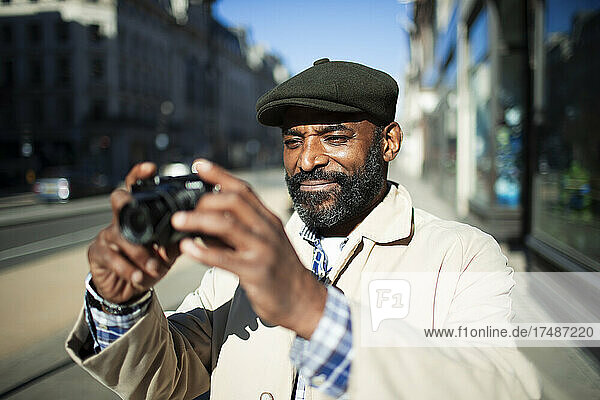 Männlicher Tourist mit Digitalkamera auf einem sonnigen städtischen Bürgersteig