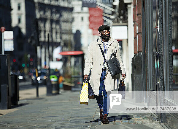 Businessman with shopping bags walking on sunny city sidewalk