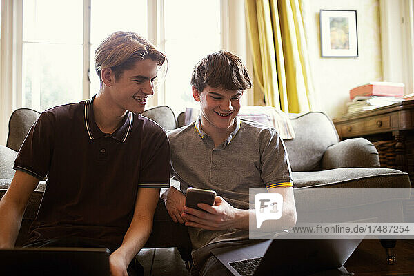Happy teenage boys with laptops studying in living room
