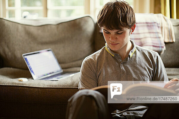 Focused teenage boy with textbook studying at home